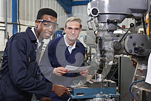 Engineer Showing Apprentice How to Use Drill In Factory