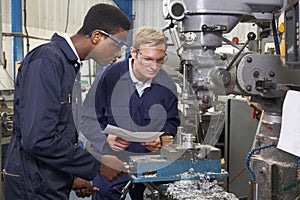 Engineer Showing Apprentice How to Use Drill In Factory