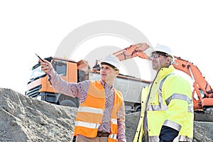 Engineer showing something to colleague while discussing at construction site against clear sky