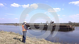 Engineer in a signal vest against the background of the river on which stands a river sand mining ship