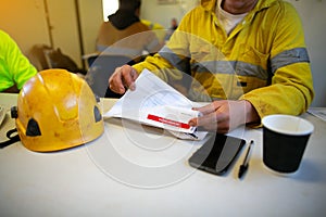 Engineer sitting placing safety hard hat on the table coffee cup pen reviewing JSA risk assessment