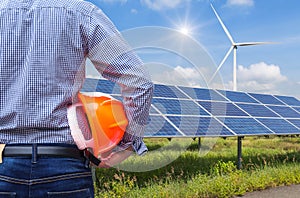 Engineer stand holding safety yellow helmet with solar cells and wind turbines generating electricity in power station