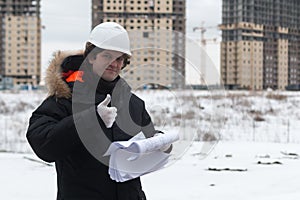 Engineer standing on the background of a new apartment building. House is built. Engineer in a helmet with papers in