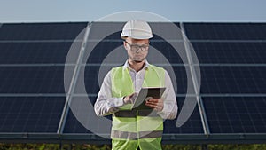 Engineer standing on farm with solar panels and using tablet.