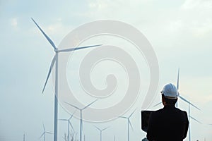 Engineer standing and hoding laptop with wind turbine photo