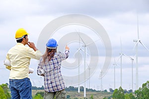 Engineer stands holding a blueprint and looks at a wind turbine project to generate electricity and check wind direction