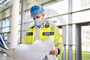 Engineer studying plan at construction site with protective face mask