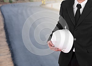 engineer in suit holding helmet with asphalt road under construction