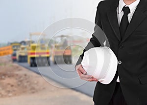 engineer in suit holding helmet with asphalt road under construction