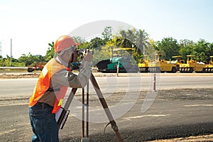 Engineer or surveyor working with theodolite equipment at road construction site.