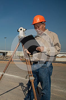 Engineer or surveyor working with theodolite equipment at road construction site.