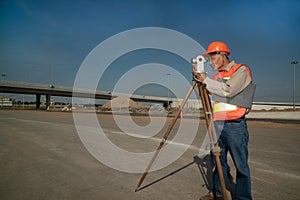 Engineer or surveyor working with theodolite equipment at road construction site.