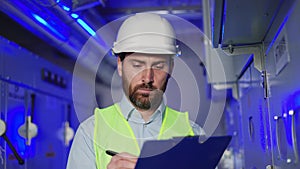 Engineer taking notes at substation checking meter data factory technical room.