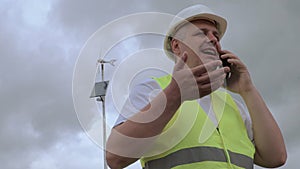 Engineer talking on smart phone near wind generator with solar panel