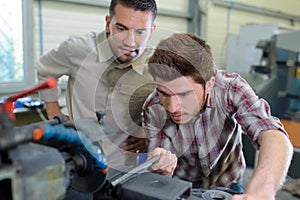 engineer teaching apprentice to use grinding machine