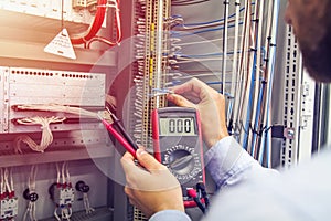 Engineer tests industrial electrical cabinet. Wire in hand of electrician with multimeter. Professional in control panel