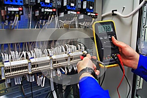 Engineer tests industrial electrical circuits with a multimeter in the control terminal box