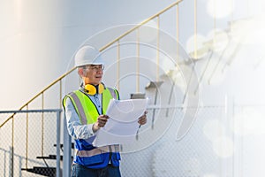 Engineer under inspection and checking oil storage tank, Engineer man in waistcoats and hardhats and with documents in oil storage