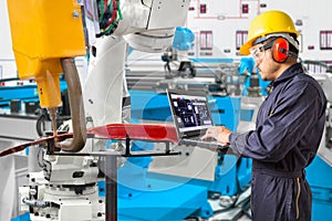 Engineer using laptop computer maintenance robot grip automotive workpiece position, Smart factory concept