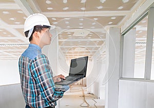 Engineer using Laptop computer and wear white safety helmet plastic in inspect interior construction