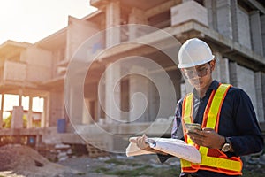 Engineer using smart phone talk with team for checking with blueprints on construction site