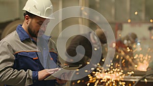Engineer using Tablet PC in in heavy industry factory. Grinding sparks background