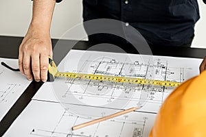 An engineer is using a tape measure to measure the plans of the house that he designs.