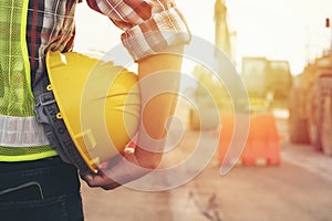 Engineer wear a hard hellmet and holding blueprint on Engineer holding helmet at road construction site with machinery background,