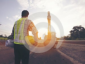 Engineer wear a hard hellmet and holding blueprint on road construction site with machinery