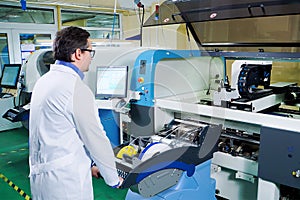 The engineer in a white robe and glasses works for the Surface Mount Technology machine. PCB Processing on CNC machine