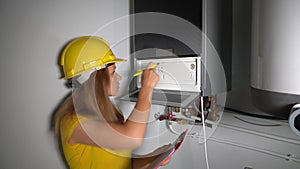 Engineer woman with helmet checking technical data of heating system equipment