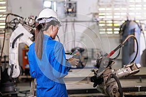 Engineer woman in uniform using remote control robotic arm machine to work in the factory. Worker setup program on the remote to