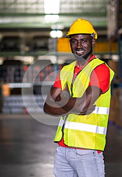 The engineer worker holds tablet crossed arm and standing in the warehouse distribution center. Man wears a safety helmet and vest