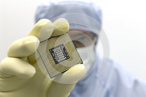 An engineer working in a clear room wearing a special uniform and protective glasses holds processor cpu in hand in glove