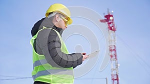 Engineer working on digital tablet, with satellite dish telecom network on telecommunication tower.