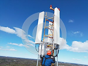 Engineer working on a telecommunications tower against the background of the blue sky.