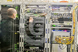 The engineer works in the server room. A man is behind a glass datacenter wall. Modern computer equipment is in server racks