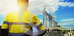 Engineer in yellow uniform, and holding a white hat, standing to look at the structure of the substation electric