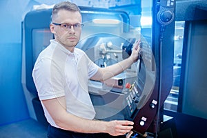 Engineer young man in glasses operates CNC automatic metalworking lathe or laser, industrial worker in modern factory