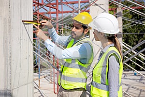 Engineer young man and woman using tape measure for check and examining length of structure at construction site.
