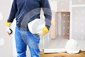 Engineering hand holding white safety hat and paper plan blueprint on wood table working interior gypsum renovate house