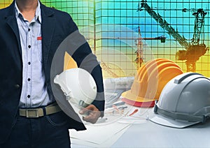 engineering man standing with white safety helmet against building and crane construction working table office use for