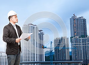 engineering man wearing western suit and safety helmet with building plan document working on high scrapper building construction