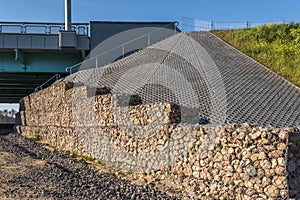 Engineering structure made of stones behind metal wire netting to strengthen the river bank near the road bridge