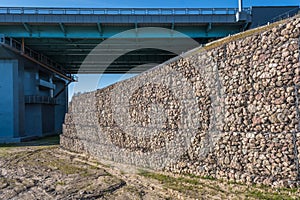 Engineering structure made of stones behind metal wire netting to strengthen the river bank near the road bridge