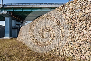 engineering structure made of stones behind metal wire netting to strengthen the river bank near the road bridge