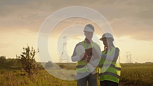 Engineering working on high-voltage tower, check the information on the tablet computer two employees man and woman.