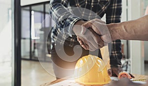 Engineers or architecture shaking hands at construction site for architectural project, holding safety helmet on their