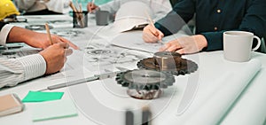 Engineers Collaborating on Mechanical Designs with Technical Drawings and Equipment, Focused Discussion in a Bright