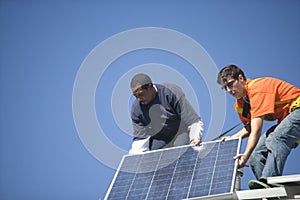 Engineers Fixing Solar Panel Against Blue Sky